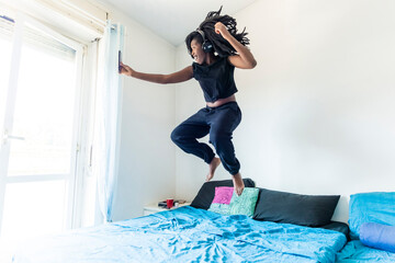 Young woman using smartphone and listening music jumping on bed