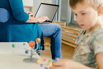 Boy exploring solar system model with woman with laptop in kindergarten
