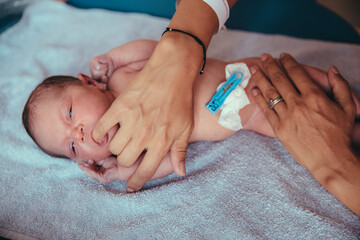 Newborn baby girl lying on towel sucking at mother's finger