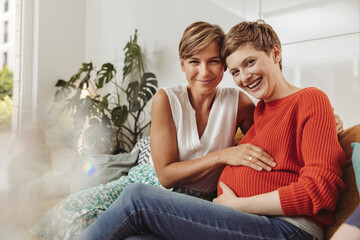 Portrait of happy lesbian couple touching belly of the expectant mother