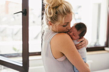 Mother holding her crying baby close to her shoulder at home