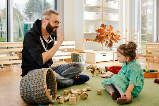 Pre-school teacher playing with girl in kindergarten