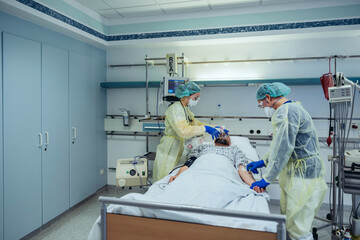 Doctors caring for patient in emergency care unit of a hospital changing breathing from oxygen mask...