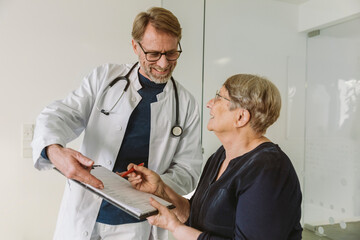 Doctor helping senior patient filling out document - obrazy, fototapety, plakaty