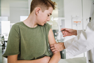Doctor injecting vaccine into arm of teenager - obrazy, fototapety, plakaty
