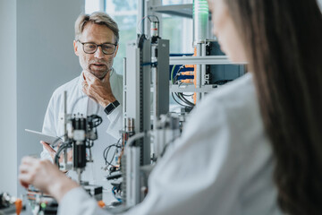 Thoughtful male scientist looking at machinery while working with female colleague in laboratory