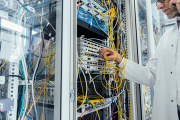 Mature man plugging in transceiver on fiber optic cable in data center