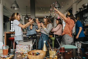 Cheerful friends throwing confetti on birthday girl while celebrating at home - Powered by Adobe