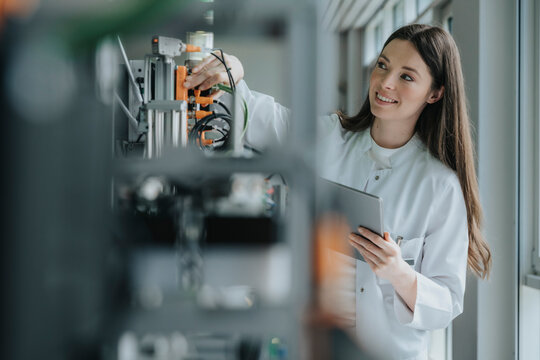 Smiling female scientist holding digital tablet inventing machinery in laboratory