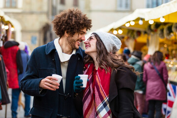 Happy affectionate young couple with hot drinks at Christmas market