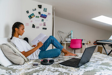 Teenage girl writing in exercise book while sitting on bed at home