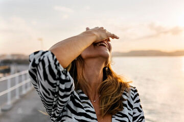 Smiling woman covering face with hand against clear sky