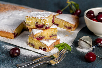 Sponge cake with cherry. Pieces of sliced sponge cake with cherry sprinkled with powdered sugar on a gray background