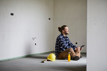 Happy worker on a construction site having a break sitting on the floor
