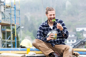 Construction worker eating salad while sitting outdoors at construction site