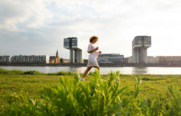 Woman with beer bottle walking on grassy land against river in city at sunset