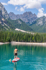 Male tourist paddleboarding on turquoise Pragser Wildsee, Dolomites, Alto Adige, Italy