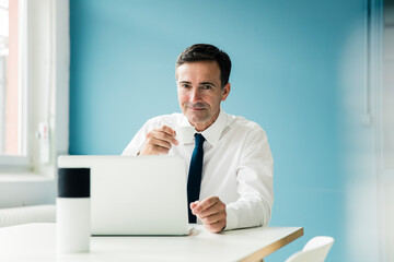 Portrait of confident businessman using laptop on table in office