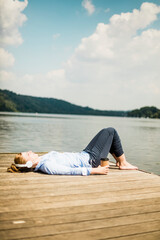 Woman lying on jetty at a lake with headphones and takeaway coffee