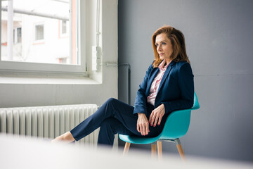 Displeased businesswoman sitting on a chair next to the window in her office