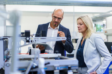 Confident businessman and businesswoman discussing while looking at machinery in factory