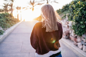 Young woman wearing fur jacket walking on street during sunset