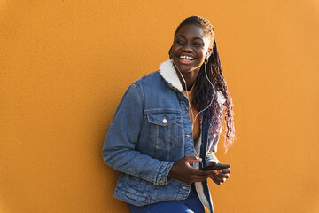 Teenage girl with mobile phone laughing while listening music against yellow wall