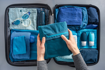 Overhead view of man packing suitcase with clothes and swimming goggles