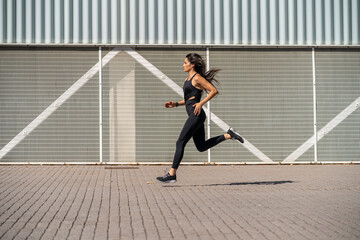 Young female jogger running in front of a wall