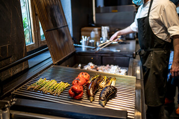 Chef wearing protective face mask preparing grilled vegetables in restaurant kitchen