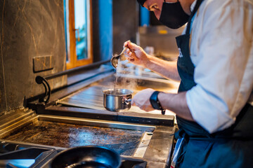Chef wearing protective face mask preparing a sauce in restaurant kitchen