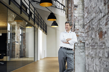 Portrait of smiling businessman leaning against brick wall in modern office