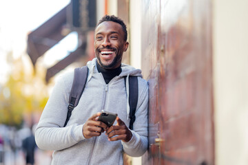 Smiling man using mobile phone while leaning on wall - obrazy, fototapety, plakaty