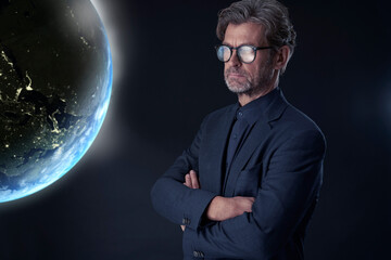 Portrait of mature businessman against dark background watching floating planet earth