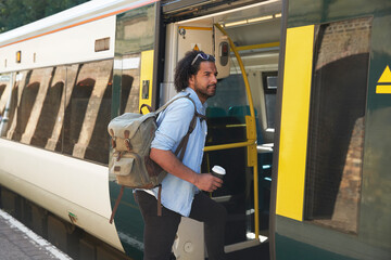Young trendy man boarding train at railroad station