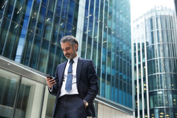 Businessman using mobile phone outside office building in city - obrazy, fototapety, plakaty