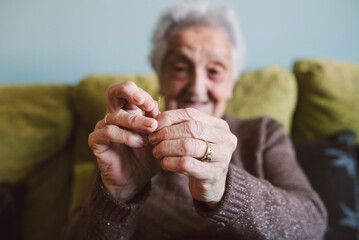Hands of senior woman sitting on couch passing thread through buttonhole of sewing needle
