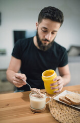 Young man preparing his breakfast at home, mixing cocoa and milk