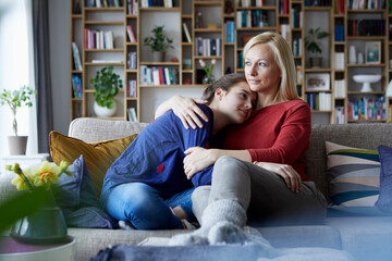 Mother and adolescent daughter sitting on couch with arms around