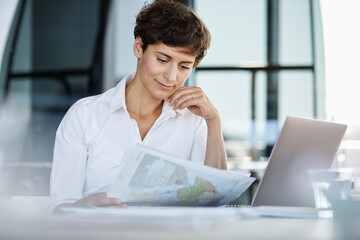 Businesswoman sitting at desk in office with laptop and document