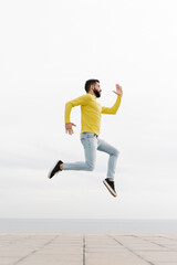 Fototapeta na wymiar Carefree young man jumping on footpath against white wall
