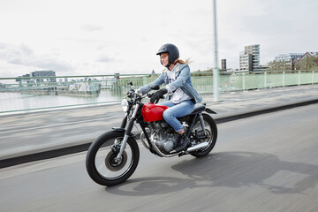 Fototapeta na wymiar Germany, Cologne, young woman riding motorcycle on bridge