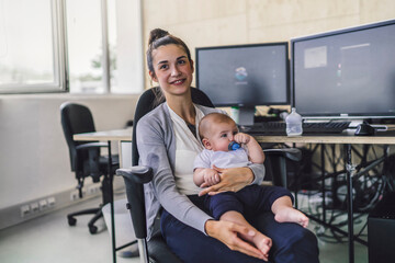 Working mother with baby on her lap, sitting in office