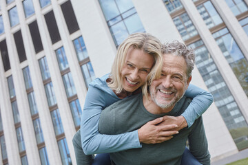 Happy mature man carrying woman piggyback in the city