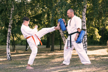 Teenage boy with instructor practicing karate at summer park