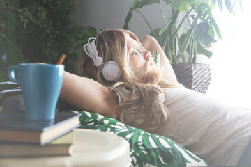 Man with long hair and beard lying on sofa listening music with headphones