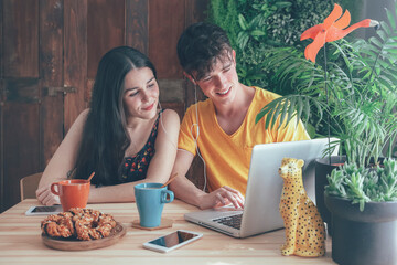 Young couple having coffee and chocolate braids using laptop at home - obrazy, fototapety, plakaty