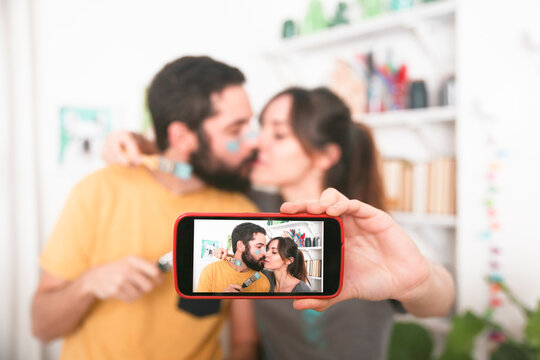 Young couple kissing and taking a selfie with paintbrushes