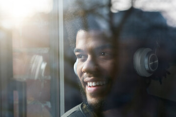 Man at window looking outside listening to music with headphones