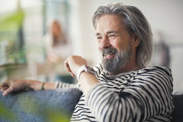 Senior man sitting on couch, talking into smartwatch - Powered by Adobe
